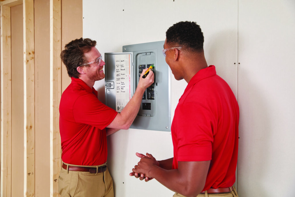 Two electricians inspecting an electrical panel and breaker box